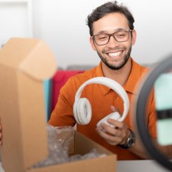 Male influencer recording a video with his cell phone in a ring of light while unboxing